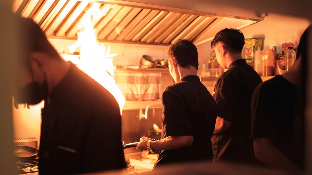 Cocina de restaurante en plena hora de servicio, con el equipo trabajando de espaldas junto al fuego de los fogones
