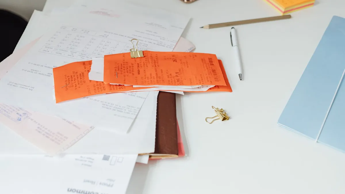 Recibos y facturas amontonados sobre un escritorio junto a un bloc de notas, el papeleo pendiente de una pyme